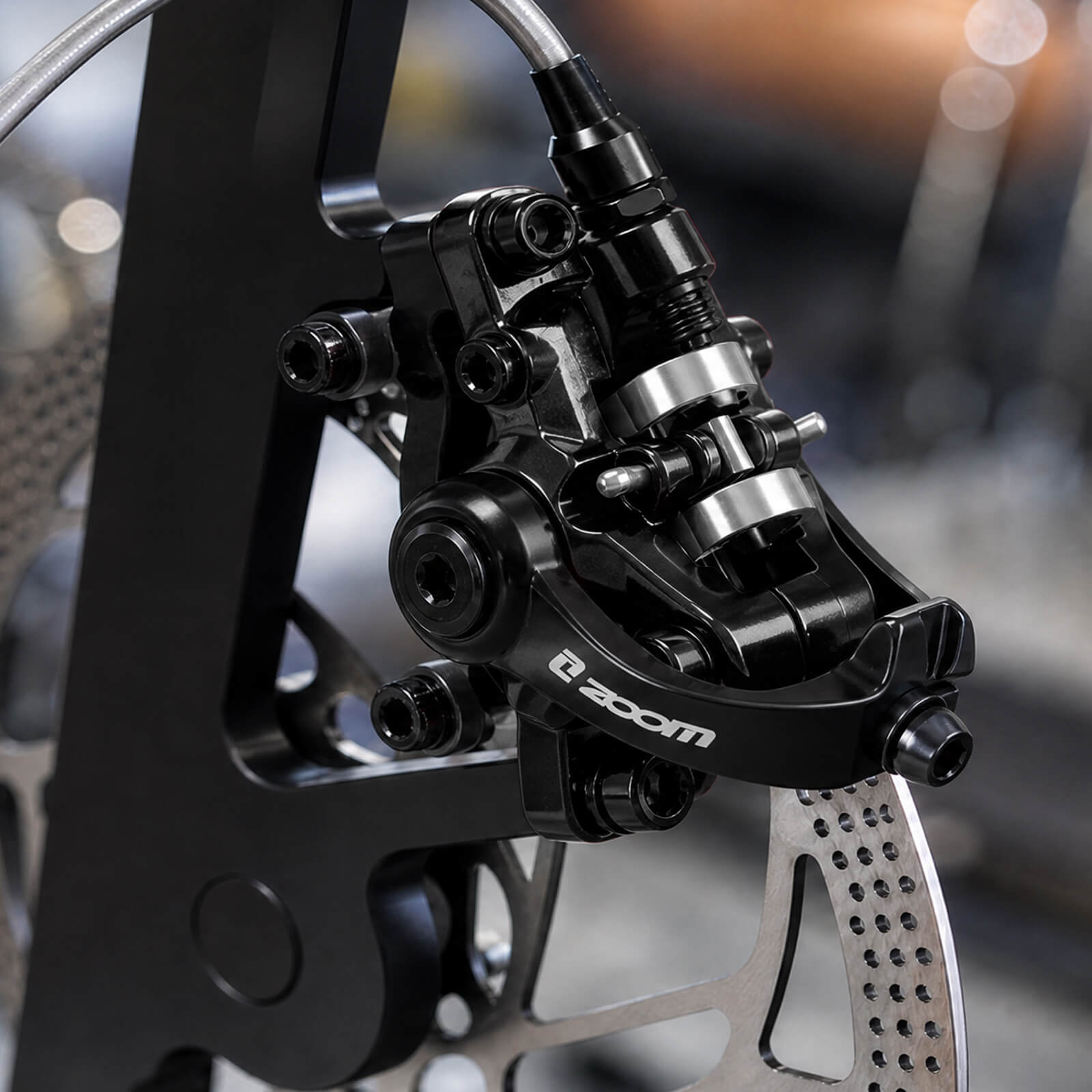 Close-up of a black ZOOM DB-680 bicycle disc brake caliper, is mounted and fixed to the silver bicycle brake rotor