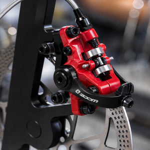Close-up of a red and black ZOOM DB-680 bicycle disc brake caliper, is mounted and fixed to the silver bicycle brake rotor